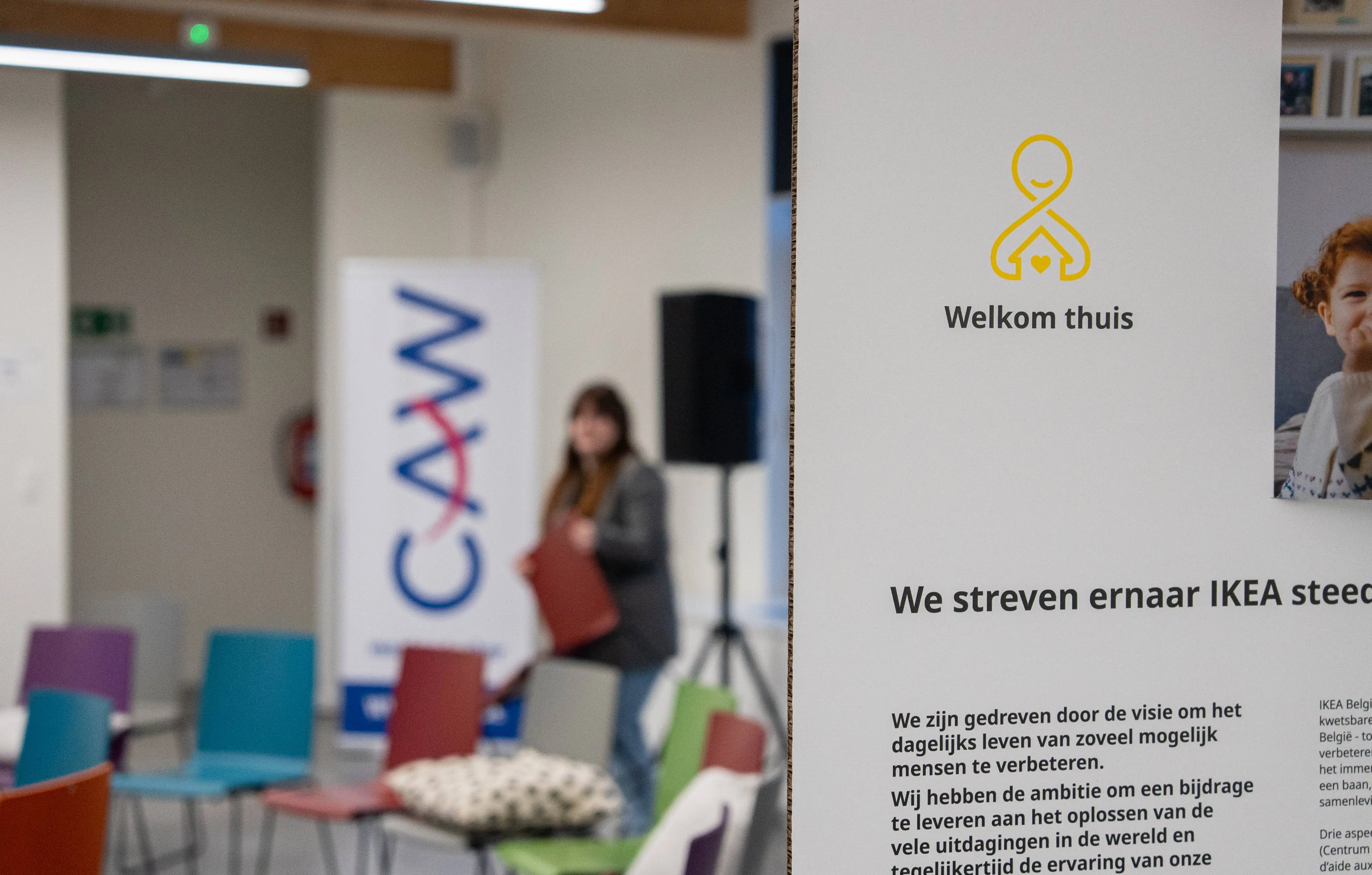 Decoratie van het evenement met de tekst “Welkom Thuis”, de naam van het project van het evenement, en op de achtergrond de lege zaal voor de aankomst van de deelnemers.